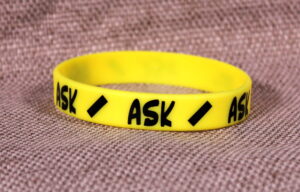 Yellow silicone wristband with "/ ASK /" printed on it.