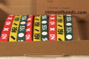 A close-up picture of three sets of 2nd-run Consentbands in "gift packaging", wrapped around a card inside a cardboard box.
